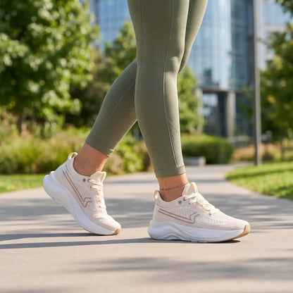 Γυναίκα που φοράει τα μπεζ αθλητικά sneakers Paredes Enix με πράσινο αθλητικό κολάν, περπατώντας σε πλακόστρωτο μονοπάτι πάρκου.
